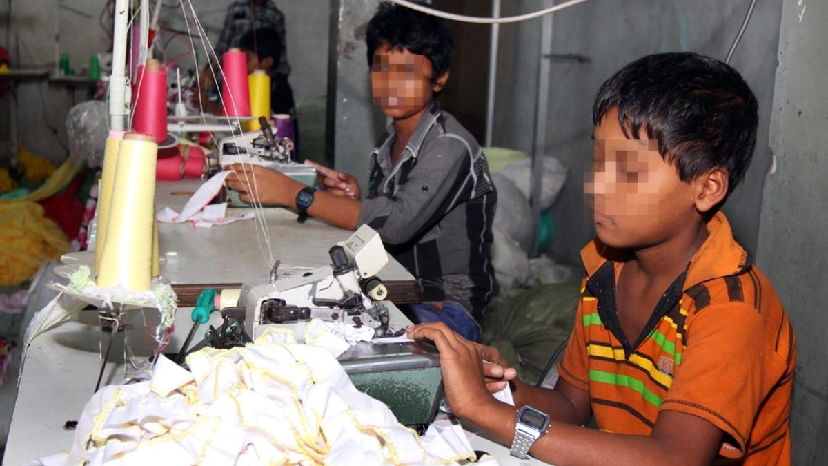 Dos niños realizan trabajos en una fábrica textil.