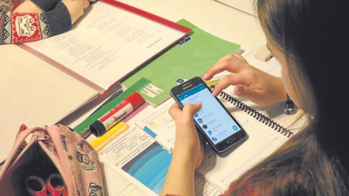 Una alumna mira el móvil mientras estudia en un aula.