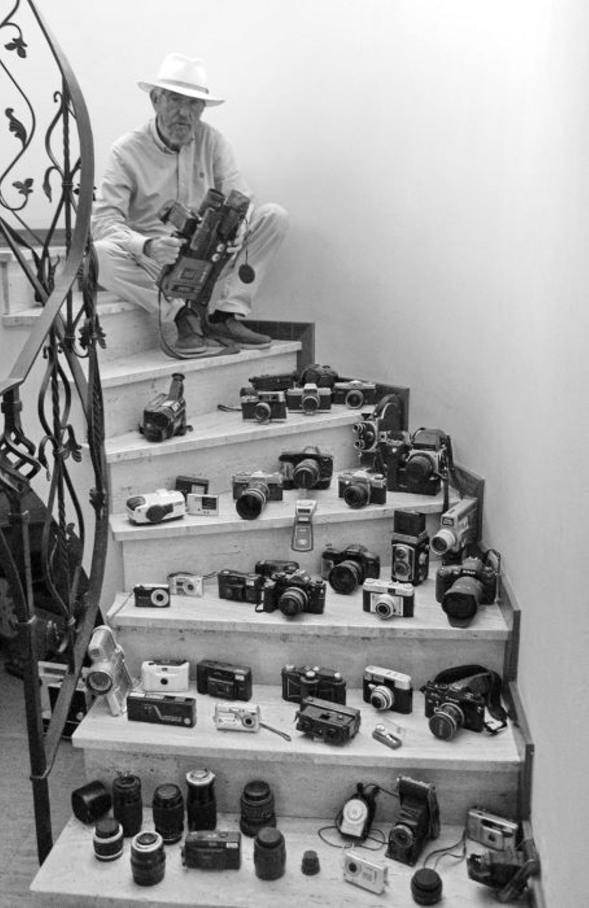 Assegut a les escales, envoltat de càmeres i objectius, en la imatge del cartell de l’exposició «Lluís Maimí. Negre sobre blanc» al Museu del Suro de Catalunya