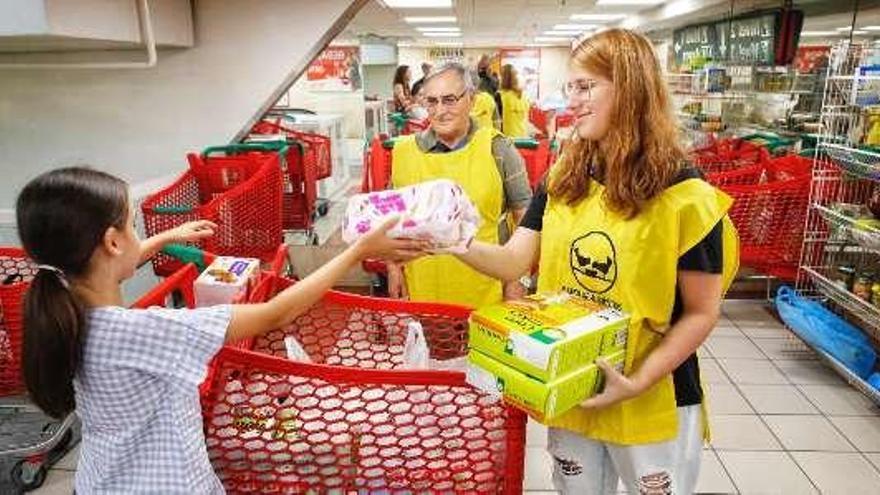 Una niña entrega alimentos a dos voluntarios. // FdV