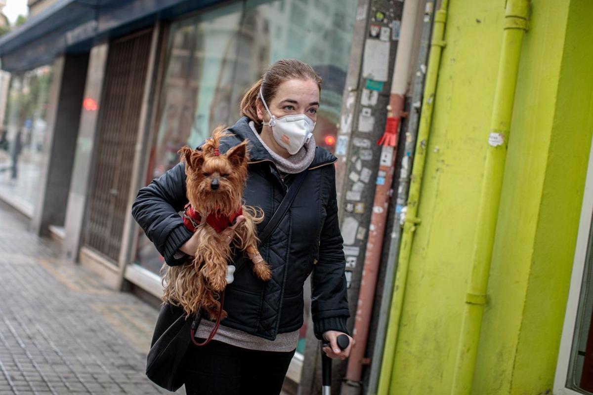 GRAFCVA3035. VALENCIA, 16/03/2020 Una persona con mascarilla camina por la calle con un perro en brazos. EFE/ Biel Aliño