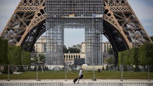 Una mujer camina con su compra frente a la Torre Eiffel, en París.