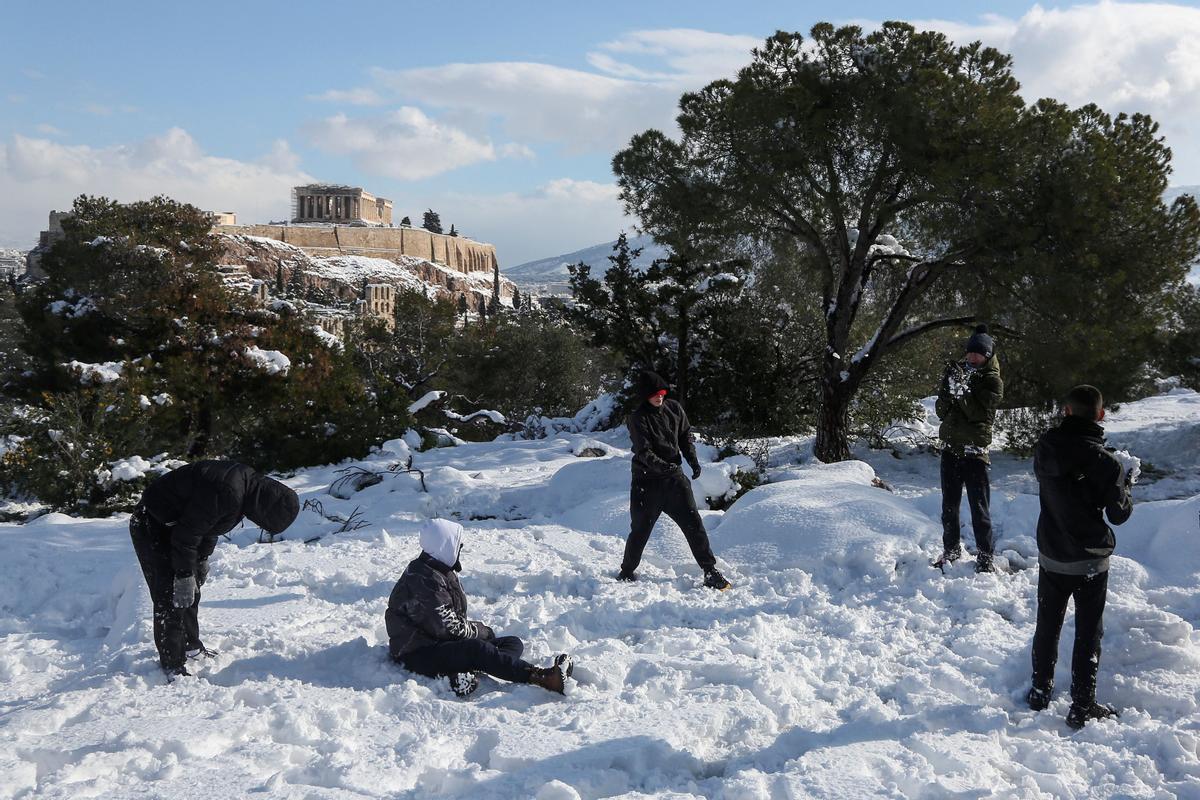 Jóvenes juegan en la colina de Filopappou, con el Partenón al fondo, tras la intensa nevada caída en Atenas.