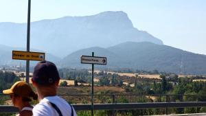 Dos turistas pasan ante la Peña Oroel cubierta por la neblina que crea el humo del incendio, este lunes.