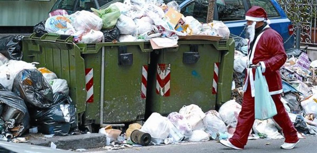En ple Nadal 8 Un home vestit de Santa Claus passa davant d’escombraries acumulades en un carrer de Nàpols.
