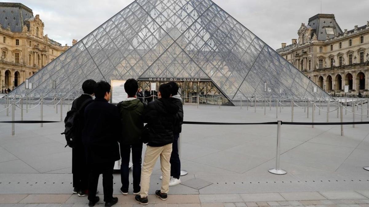 Un grupo de turistas frente la pirámide del Louvre.