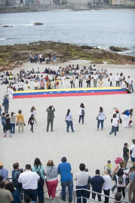 La comunidad venezolana despliega en la playa de Riazor una bandera para exigir que su país sea "libre".