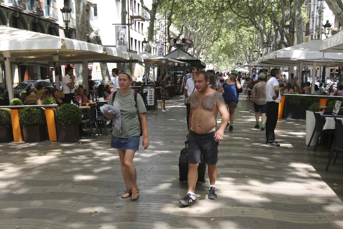 Una persona camina sin camiseta por La Rambla de Barcelona.