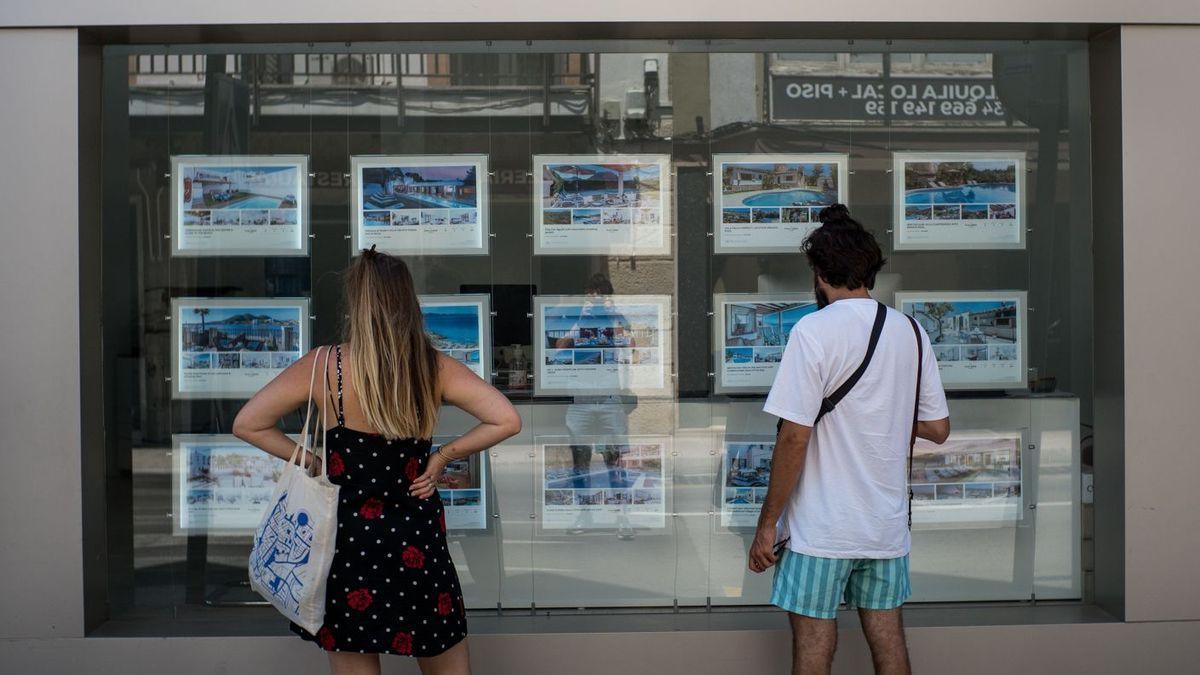 Dos personas observan anuncios en una inmobiliaria.