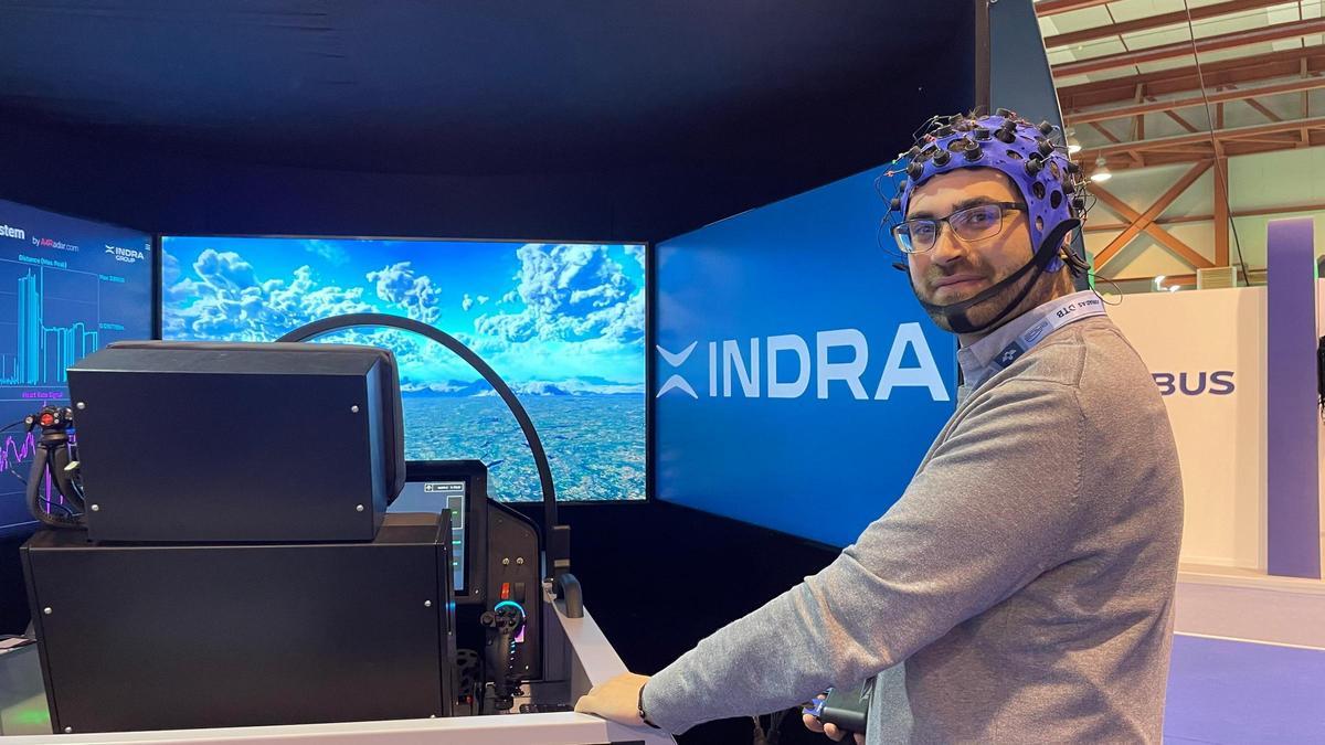 El técnico de Indra Álvaro Travesedo, con un prototipo de neurocasco para pilotos de aviones militares y ante un simulador de vuelo de su compañía