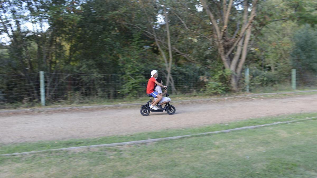 Dos chavales en un patinete eléctrico circulando por el carril bici del Prado de las Pavas.