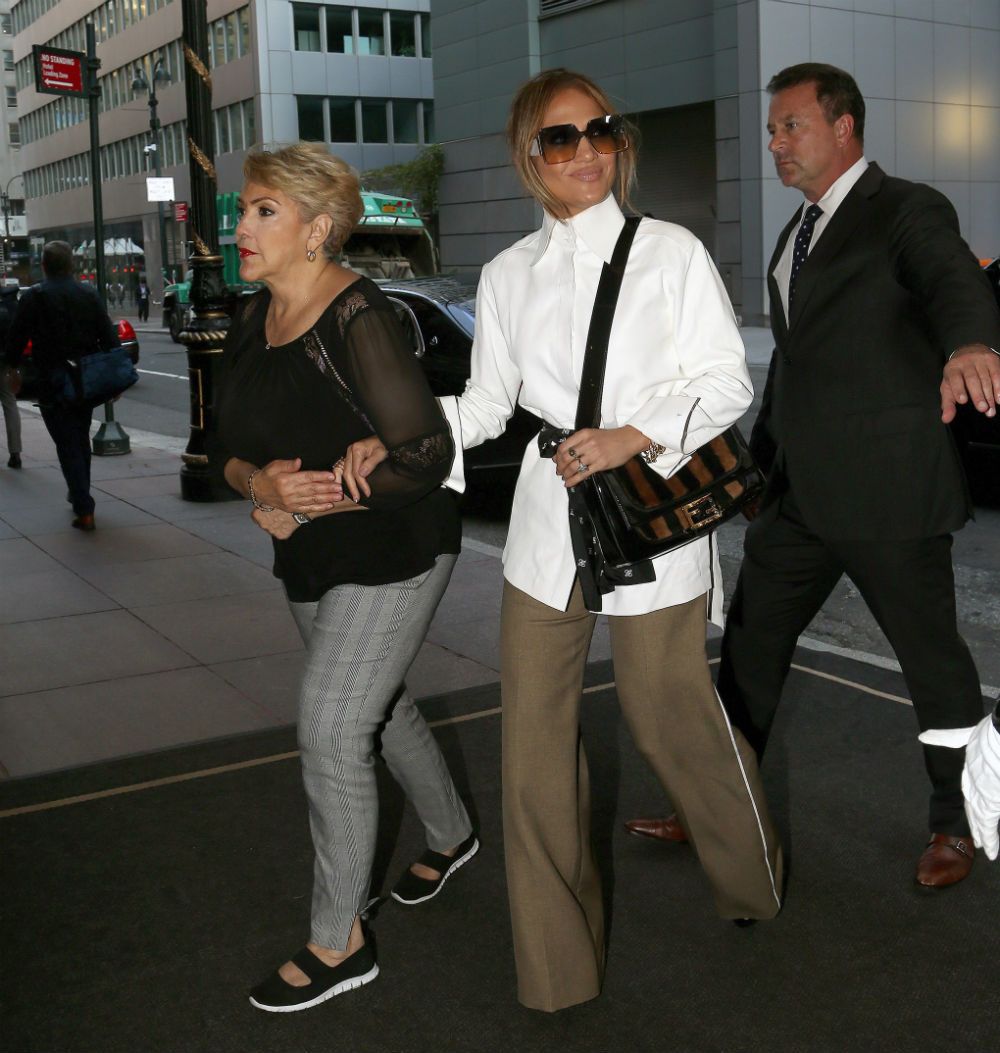 Jennifer López con camisa blanca, pantalón de pata de elefante y bolso