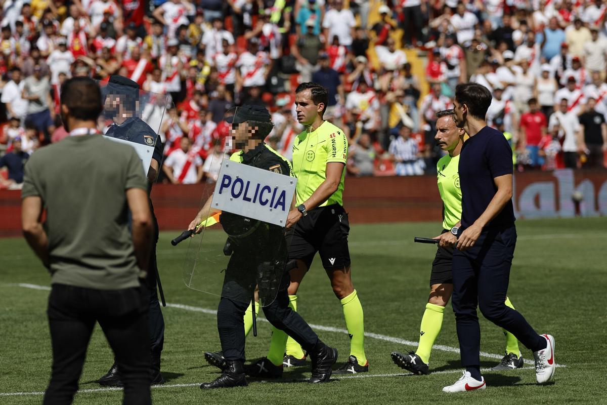 El arbitro José Luis Guzmán Mansilla sale escoltado por la policiía mientras escucha las quejas del entrenador del Rayo Vallecano Íñigo Pérez
