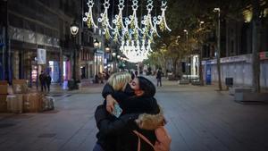 Dos amigas se dan un abrazo bajo las luces de Navidad del Portal de l’Àngel, en Barcelona.