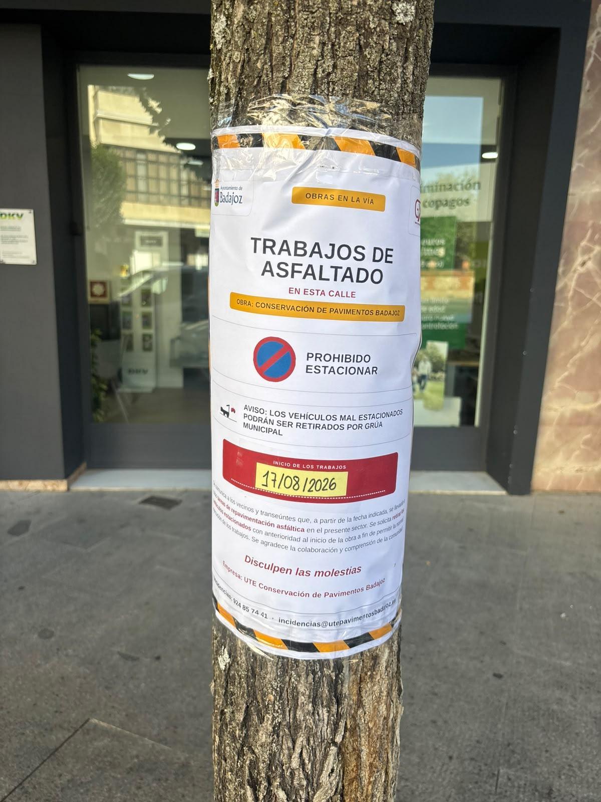 Cartel instalado en árboles y farolas informando de los trabajos de asfaltado en la calle Pedro de Valdivia de Badajoz.