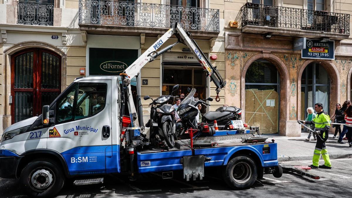 Una grúa retira motos de la calle, en el centro de Barcelona, para dejar espacio para montar las paradas de Sant Jordi.