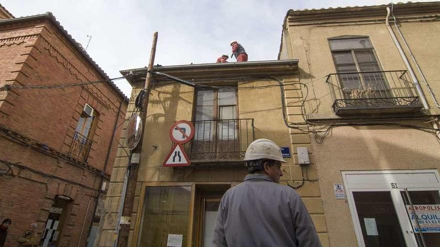 Dos operarios trabajan en la cubierta del edificio mientras un tercero vigila la caída de restos hacia la calle Herreros.