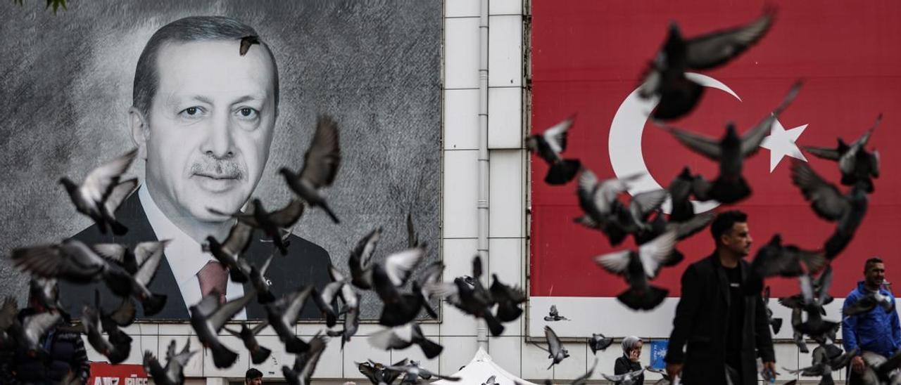 Una bandada de palomas alza el vuelo en una plaza decorada con un retrato del presidente turco, Recep Tayyip Erdogan.