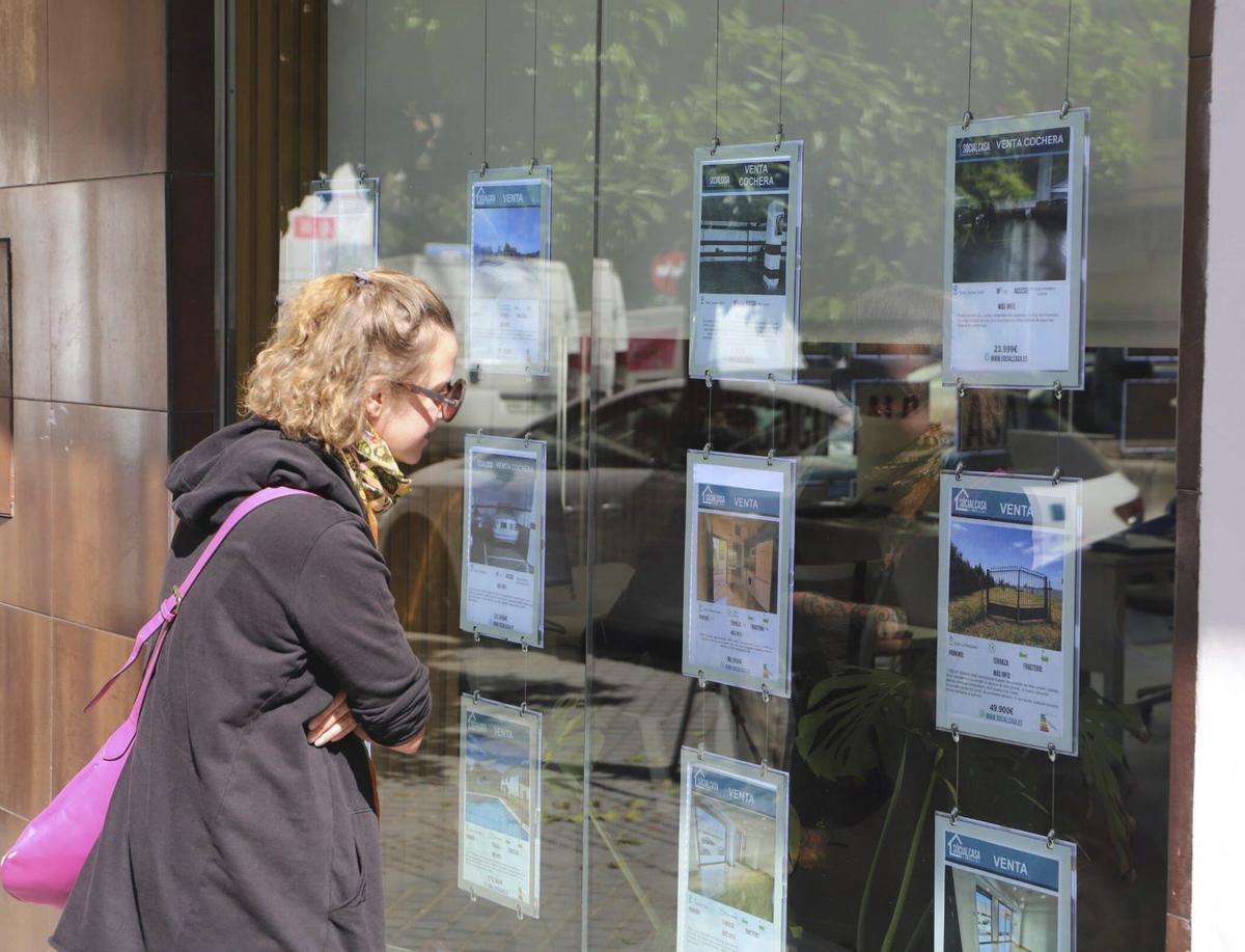 Una mujer observa varias viviendas en el escaparate de una inmobiliaria de Córdoba capital.