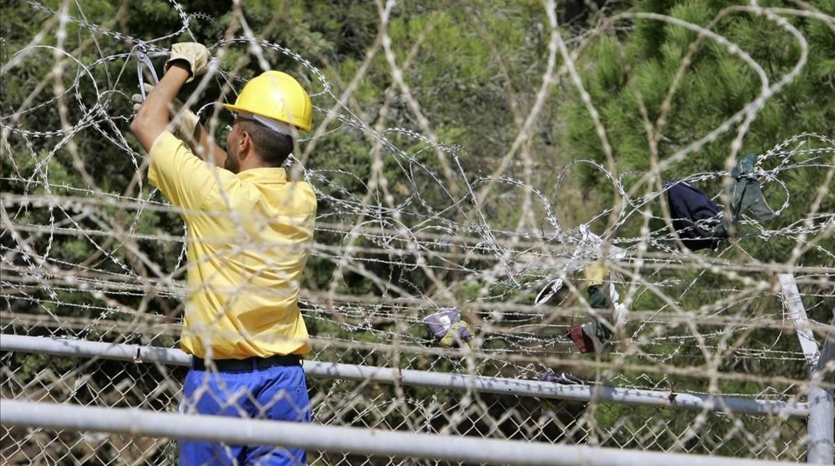 Un trabajador repara la barrera de alambradas de Melilla, tras un intento de inmigrantes africanos por superarla desde Marruecos, el 5 de octubre del 2005.