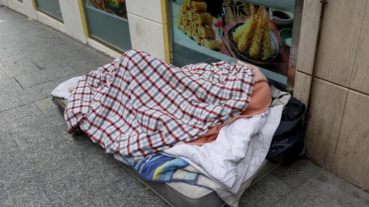 Una persona sin hogar duerme tapada por mantas en una calle de Madrid.