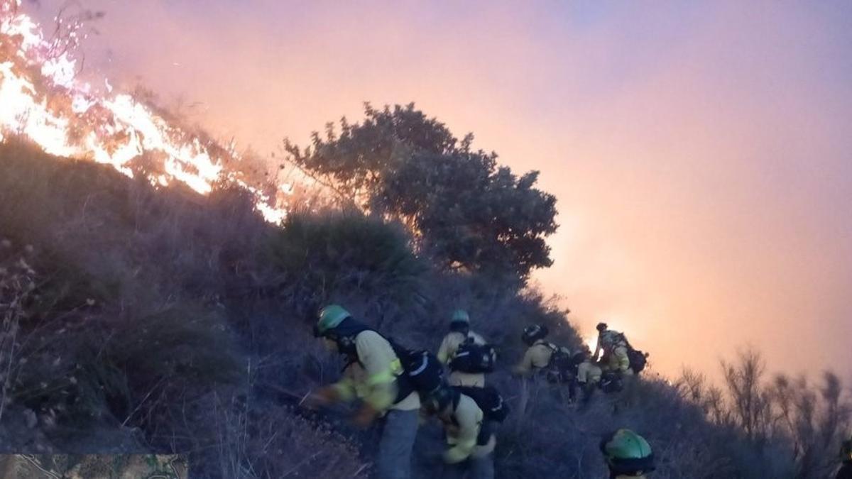 Bomberos del Plan Infoca trabajan para sofocar las llamas en las escarpadas laderas de Peña Escrita.