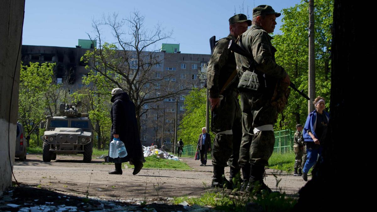 Residents walk in the city of Mariupol as the self-proclaimed Donetsk People's Republic (DNR) servicemen guard an area on April 29, 2022, amid the ongoing Russian military action in Ukraine. (Photo by Andrey BORODULIN / AFP)
