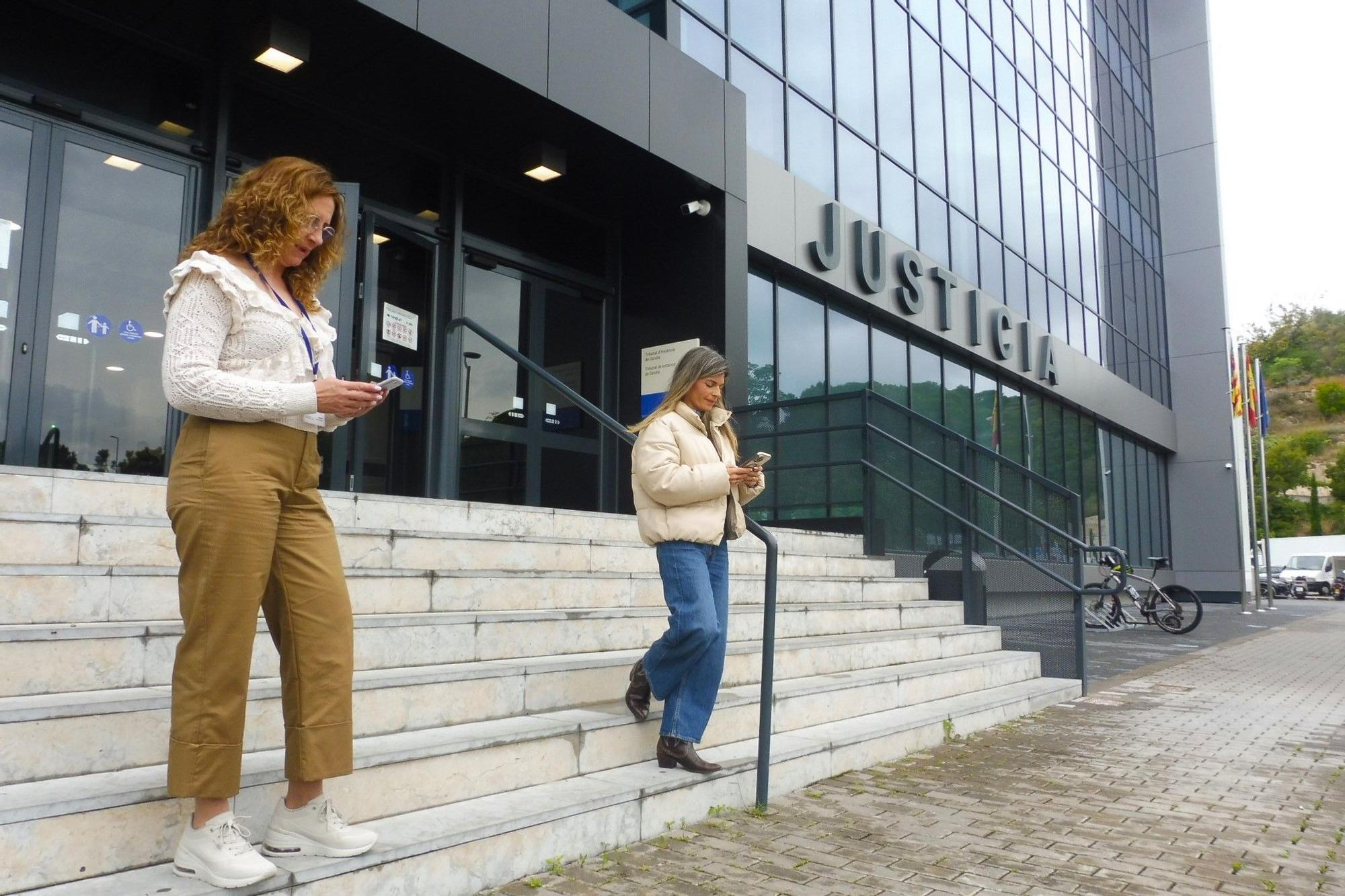 Dos funcionarias buscan cobertura en la calle, en la puerta principal del Palacio de Justicia de Gandia, este viernes.