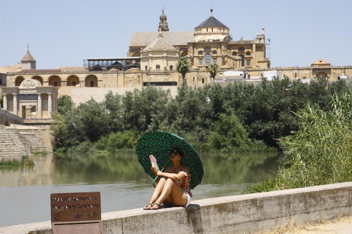 Una turista se protege del calor con un paraguas y un abanico en Córdoba.