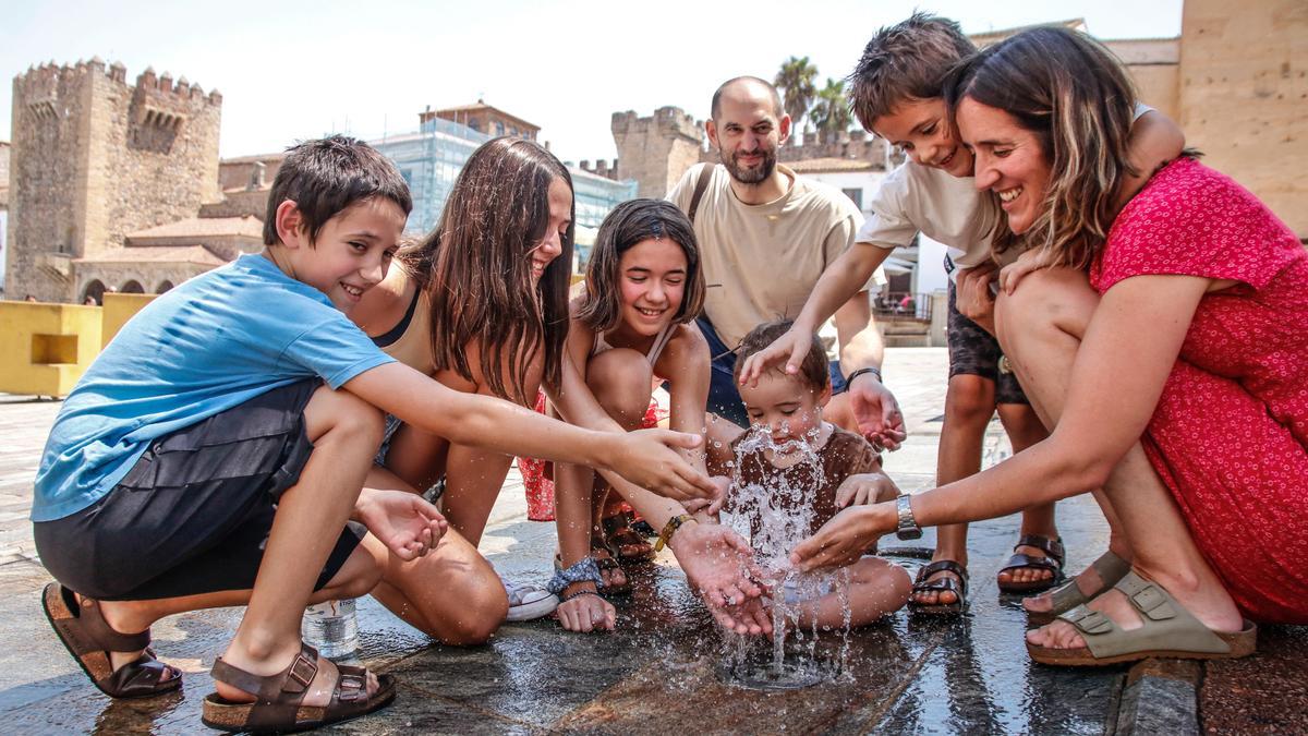 Una familia de El País Vasco se refresca en la fuente de la plaza Mayor de Cáceres.