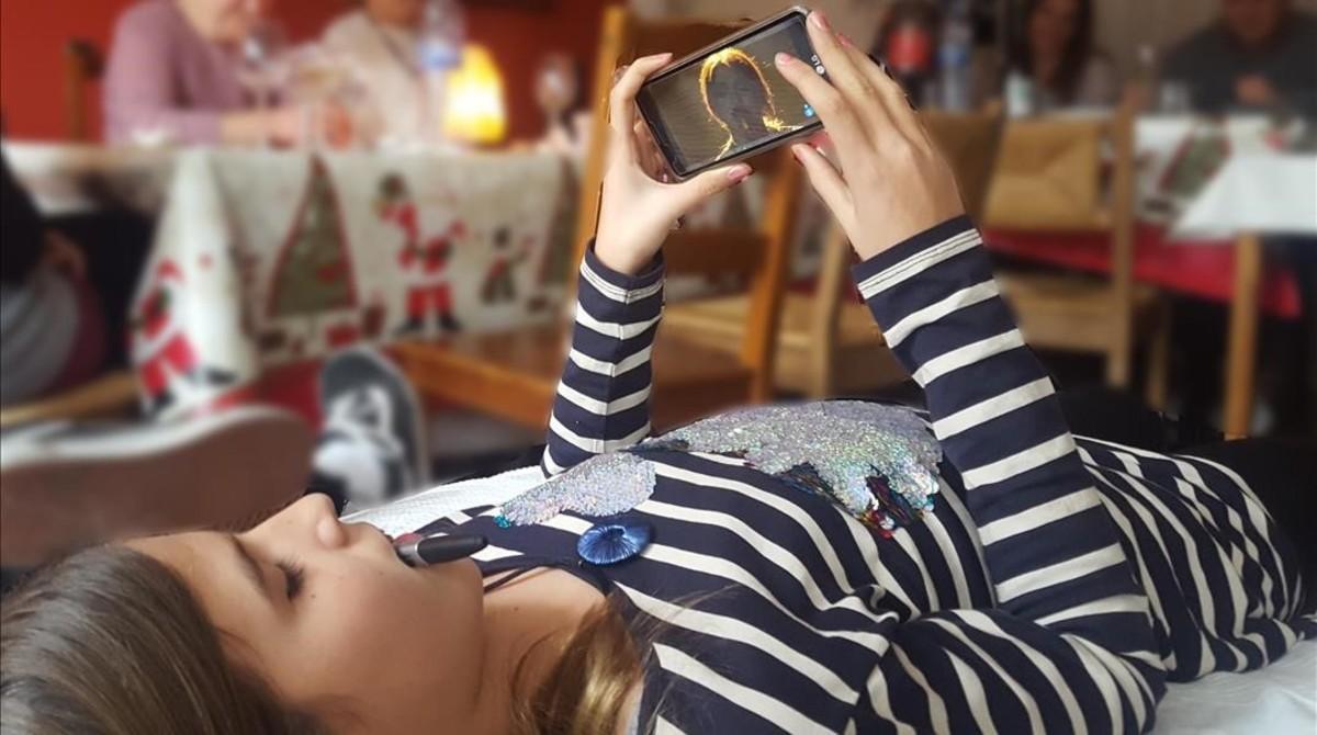 Una niña utilizando el teléfono móvil durante una comida familiar.