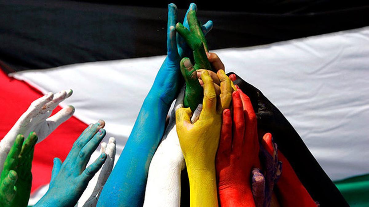 Un grup d’escolars libanesos uneixen les mans pintades davant d’una bandera palestina a la ciutat portuària de Sidó.