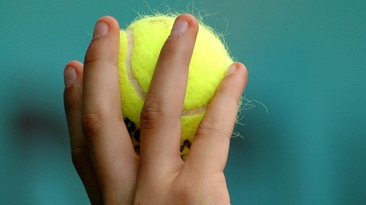 Una persona sostiene una pelota de tenis.