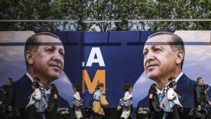 Ciudadanos caminan frente a un poster electoral de Erdogan. 