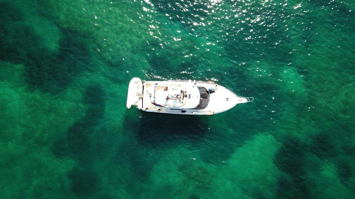 Una embarcación navega sobre las cristalinas aguas que transparentan la pradera de posidonia oceánica
