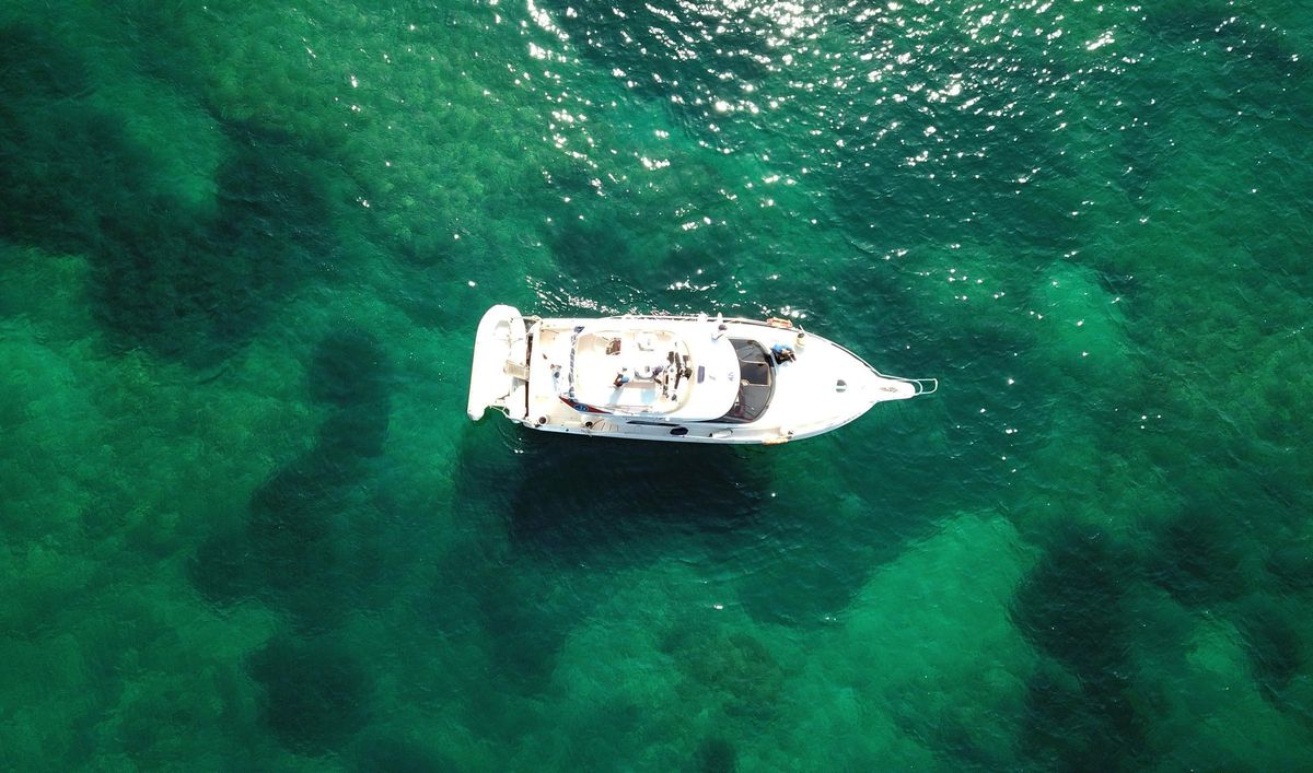 Una embarcación navega sobre las cristalinas aguas que transparentan la pradera de posidonia oceánica