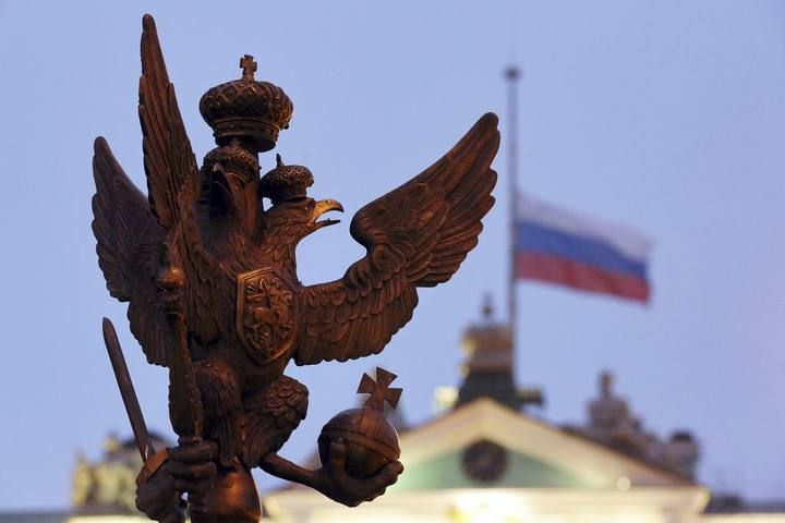 A sculpture of a double-headed eagle, a national symbol of Russia, is seen in front of a Russian national flag flying at half-mast on the roof of the State Hermitage Museum in St. Petersburg