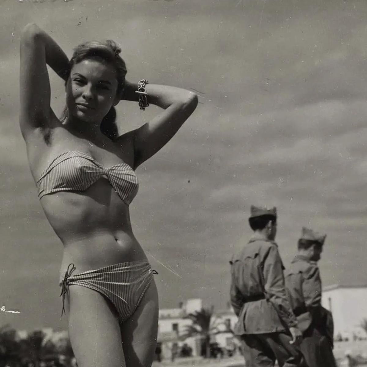 Una mujer posa en bikini con dos guardias franquistas detrás.