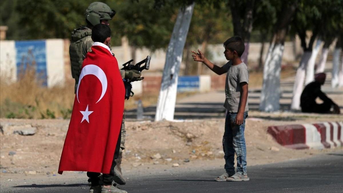 Un niño con una bandera de Turquía camina junto a un soldado turco en la ciudad de Tal Abyad.