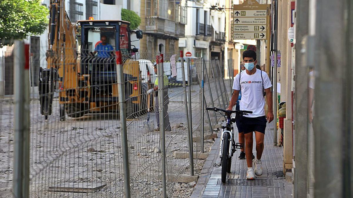 Un joven ciclista camina por el acerado delimitado con motivo de las obras de la calle Puerta de Aguilar.