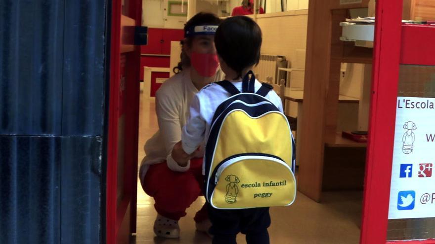 Un infant amb la mestra a l&#039;entrada de l&#039;escola infantil Peggy de Barcelona, després de xafar un drap amb desinfectant, el dia en què reobren les escoles bressol privades de la ciutat