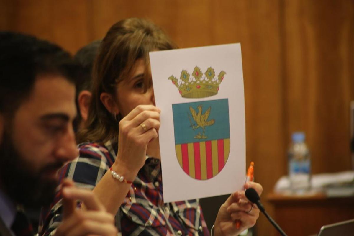 La edil de Festividades, Mariola Rocamora, muestra en el pleno la imagen del nuevo escudo de Orihuela
