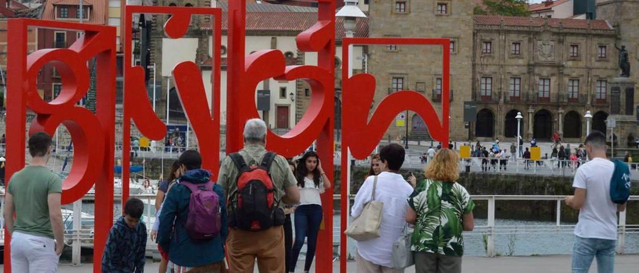 Turistas haciéndose fotos ante las &quot;letronas&quot;, con Cimadevilla al fondo.