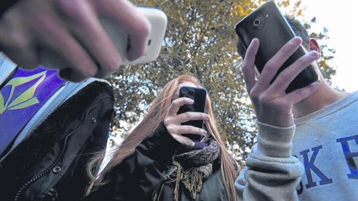 Un grupo de jóvenes consultan aplicaciones de sus teléfonos móviles, en Barcelona.