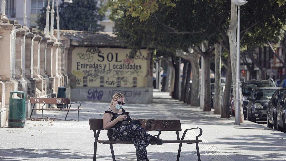 Una mujer mira el móvil con mascarilla frente a la Plaza de Toros.