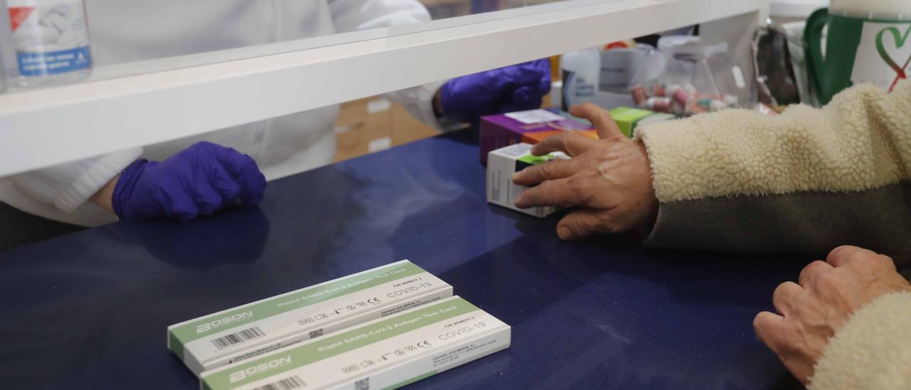 Una farmacia de València vende varios test de antígenos a una clienta.