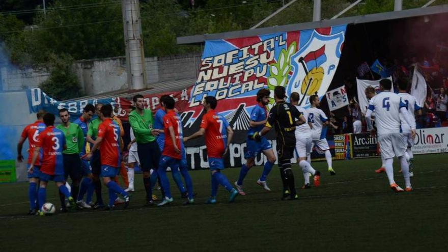 Los jugadores de ambos equipos se saludan antes del inicio del partido ante el tifo desplegado por los aficionados del Langreo.
