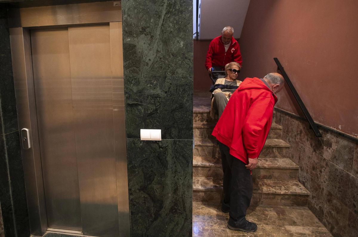 La Cruz Roja ayuda a Pepita, de 88 años, a salir a la calle. Desde hace cinco meses no tienen ascensor y ella va en silla de ruedas.