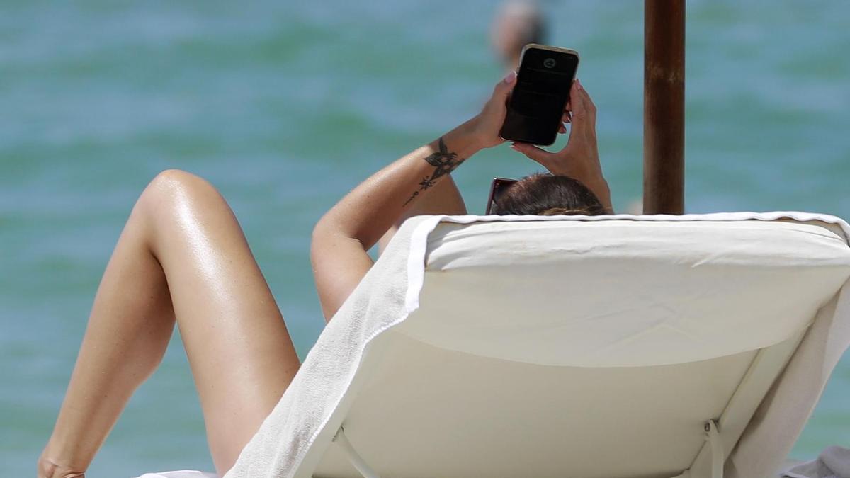 Eine Frau schaut auf ihr Handy, während sie einen Sonnenbad am Strand nimmt. Foto: Clara Margais/dpa