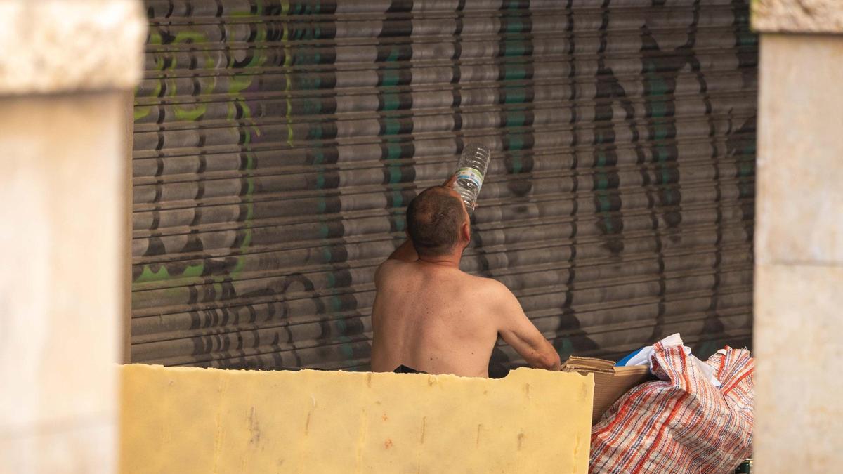 Una persona sin hogar, sin camiseta e hidratándose en Zaragoza durante la segunda ola de calor del verano.